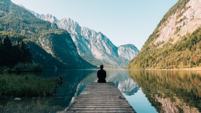 a person sitting on wooden planks across the lake scenery